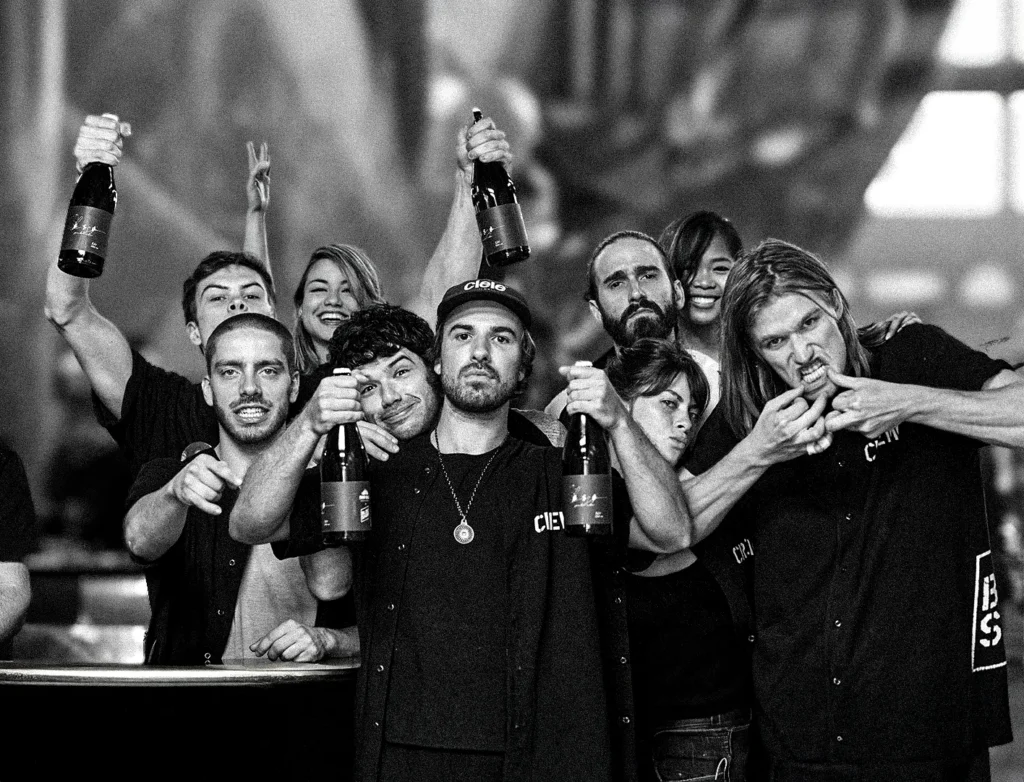 Un groupe de jeunes font des signes à la caméra avec bouteilles de bières à la main.